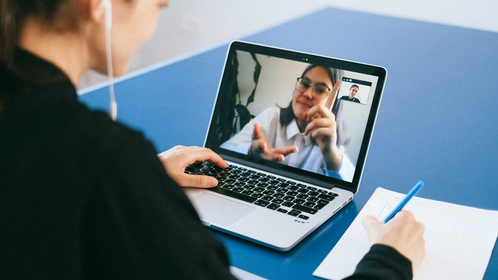 Woman participating in a virtual meeting, taking notes during a video conference on a laptop.
